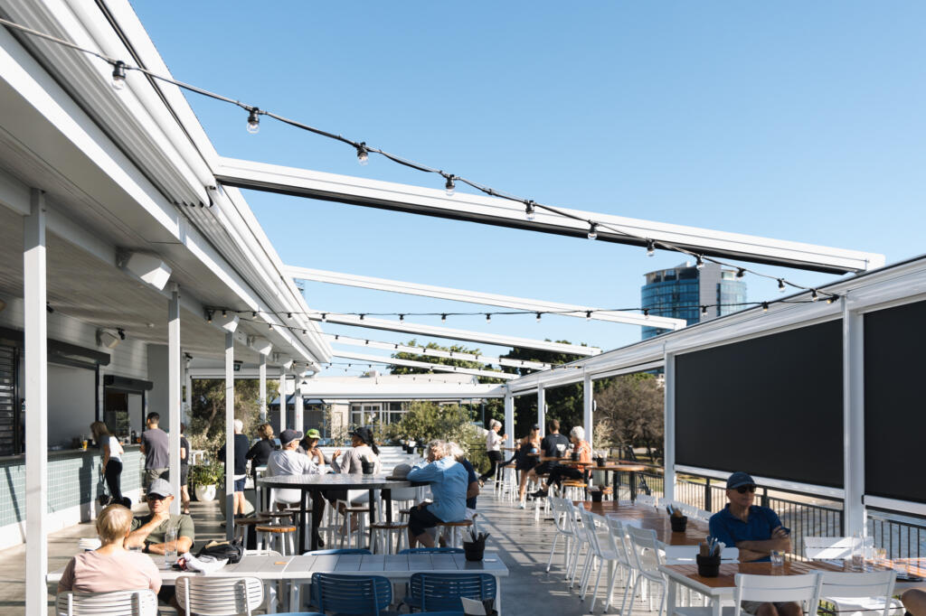Outdoor dining area with white retractable roof beams and café blinds overlooking river views