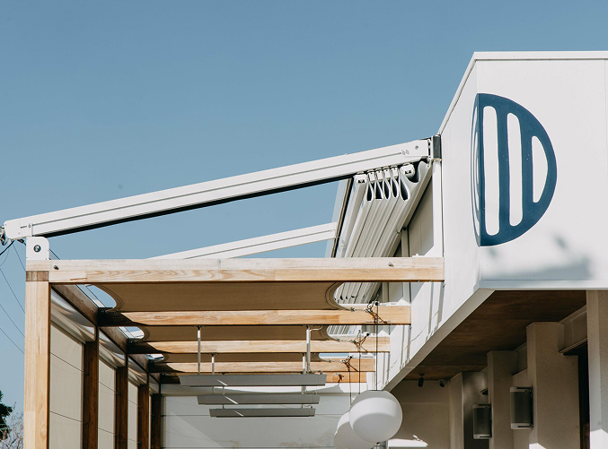 Commercial retractable roof system mounted on timber beams with branding visible on building façade