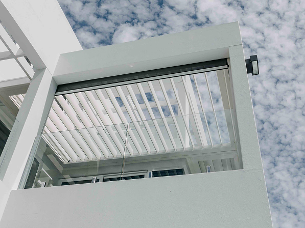 Modern white pergola with adjustable louvre roof and glass balustrade, installed on a residential balcony
