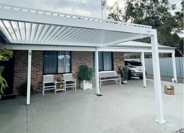 White louvre roof installed over front patio and driveway of brick home with outdoor seating